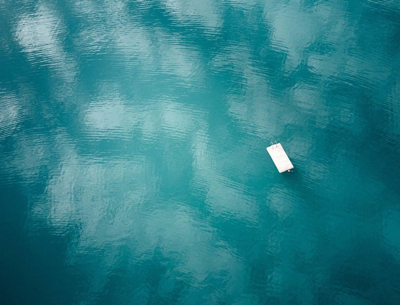 Floating wooden dock on calm turquoise lake with sky reflections