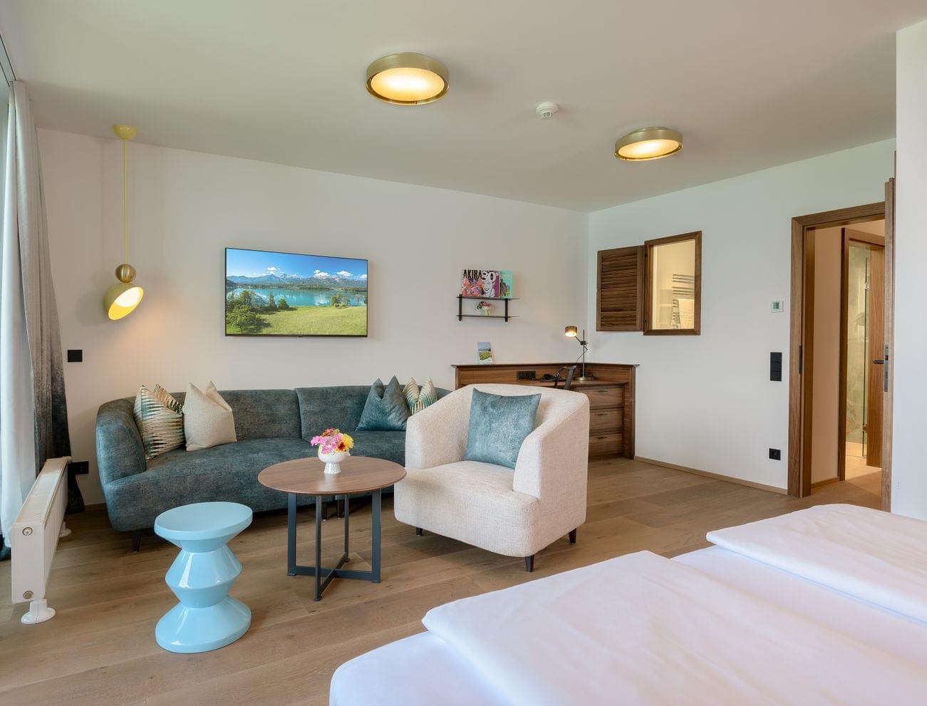 Modernes Hotelzimmer mit Sofa, Sessel, Schreibtisch, Fernseher und Holzfußboden