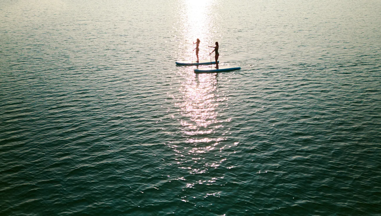 Zwei Personen beim Stand-Up-Paddeln auf ruhigem Wasser im Sonnenuntergang