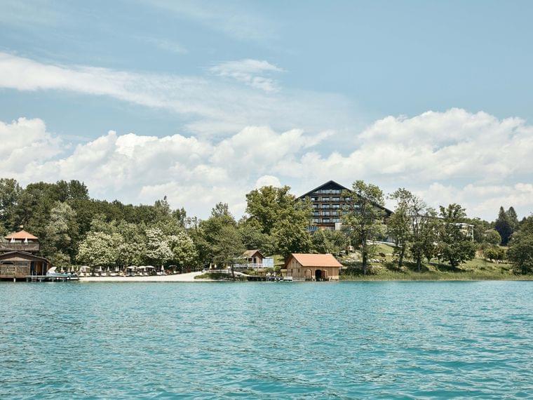 Hotel am Seeufer umgeben von Bäumen mit Bootshäusern und klarem blauem Wasser