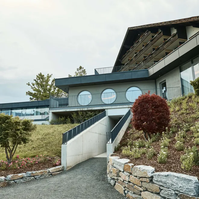 Modernes Hotelgebäude mit runden Fenstern und angelegtem Garten am Hang