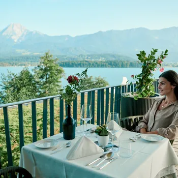 Frau beim Essen auf einem Balkon mit Blick auf See und Berge