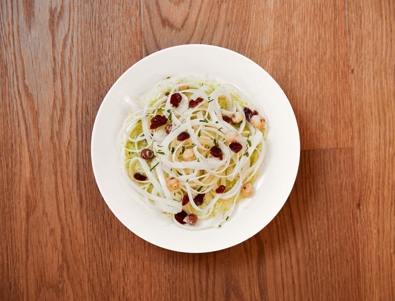 White pasta with pesto sauce, cranberries, and hazelnuts in a white bowl on wooden table