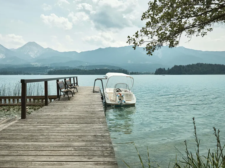 Molo in legno con panche e barca bianca su lago alpino limpido con montagne sullo sfondo