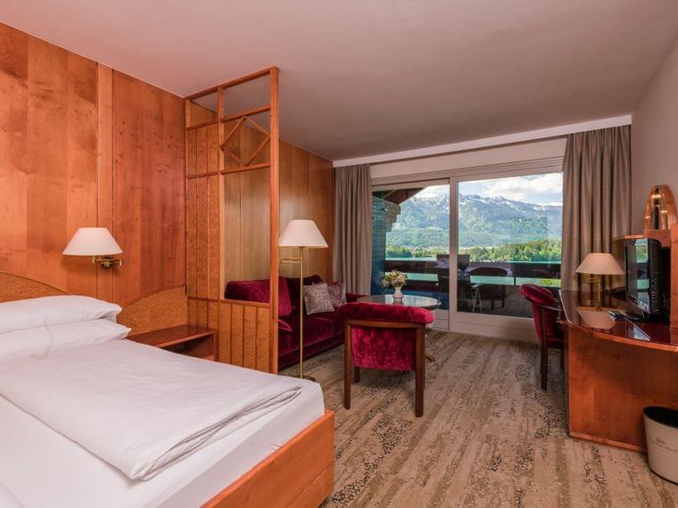 Accogliente camera d'hotel con arredi in legno, sedute in velluto rosso e vista montagna dal balcone