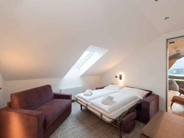 Moderna camera d'hotel mansardata con divano letto, lucernario e vista sul balcone con paesaggio montano