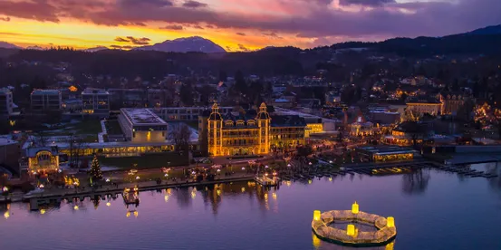 Weihnachtsbeleuchtung an Gebäuden am Wörthersee in Velden bei Sonnenuntergang mit Bergpanorama
