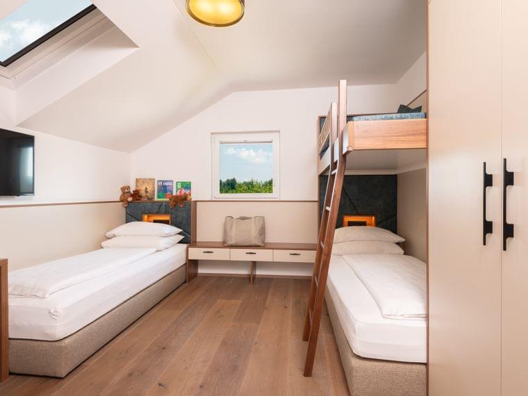 Modernes Familienzimmer mit zwei Einzelbetten und einem Etagenbett unter Dachfenster