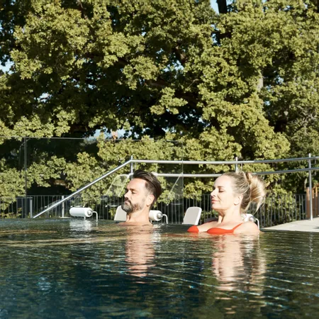 Couple relaxing in outdoor infinity pool with forest view in sunny weather