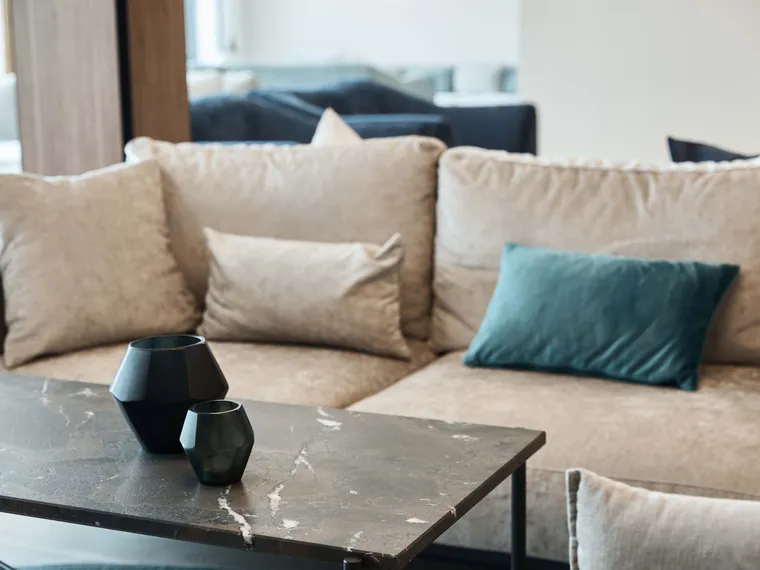 Modern beige sofa with velvet cushions and black geometric vases on a marble coffee table