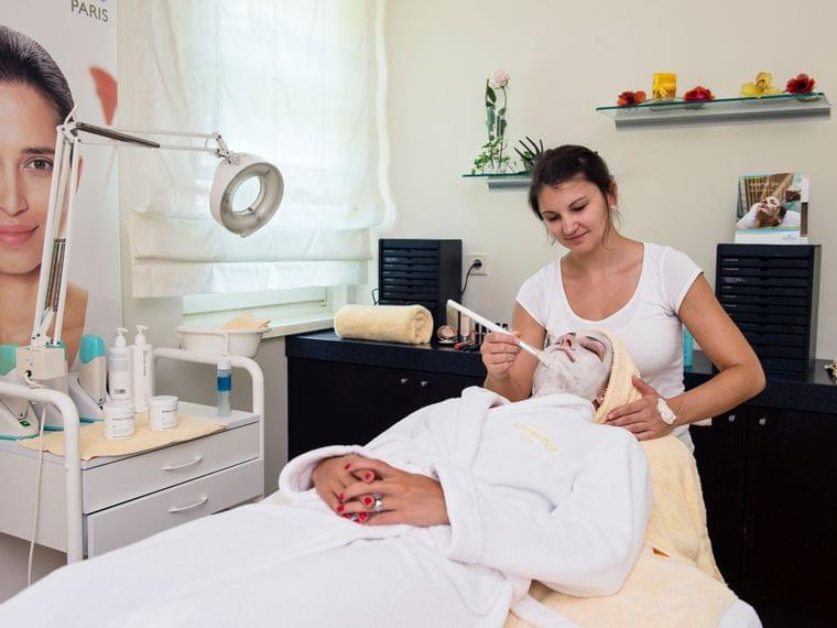 Estetista applica maschera viso a donna in sala trattamenti spa
