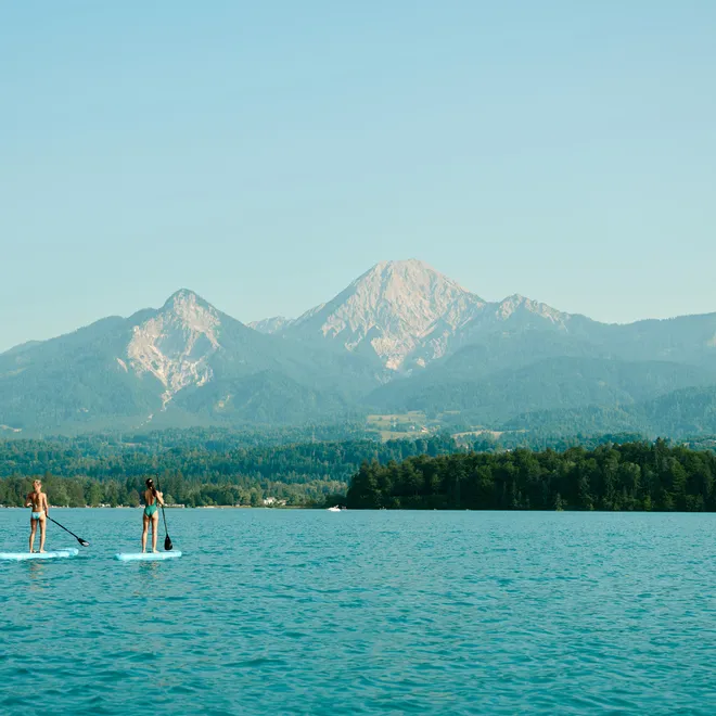Zwei Personen beim Stand-Up-Paddeln auf einem See mit Bergkulisse im Hintergrund