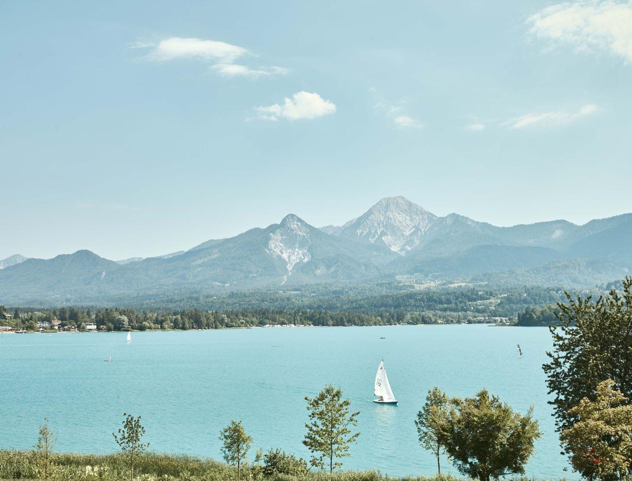 Sailboat on turquoise alpine lake with forested mountains in the background