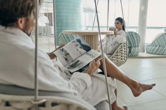 Couple relaxing in spa lounge chairs with robes, reading and drinking tea