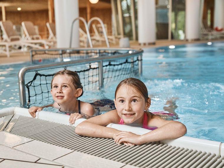 Due bambini sorridenti in una piscina coperta aggrappati al bordo