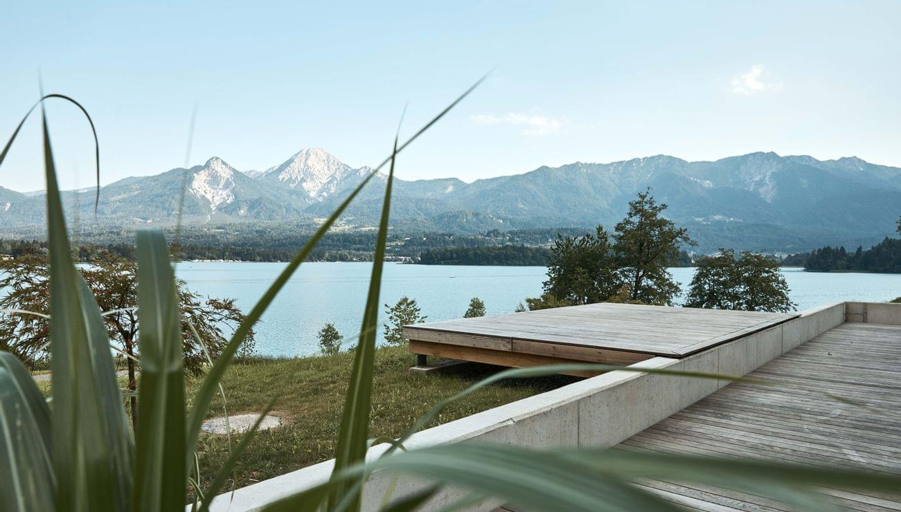 Moderna terrazza in legno con vista su lago alpino e montagne in una giornata limpida
