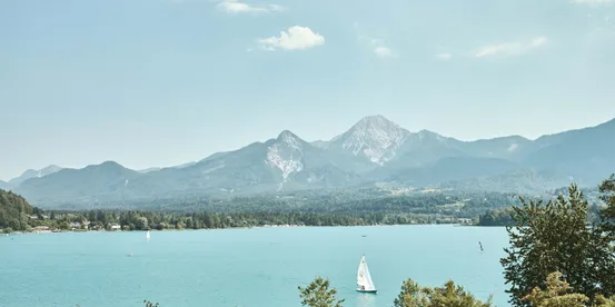Barca a vela su lago alpino turchese con montagne boscose sullo sfondo