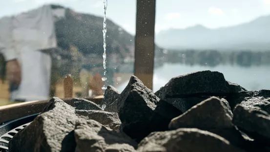 Wassertropfen auf heiße Saunasteine mit Bergen und See im Hintergrund