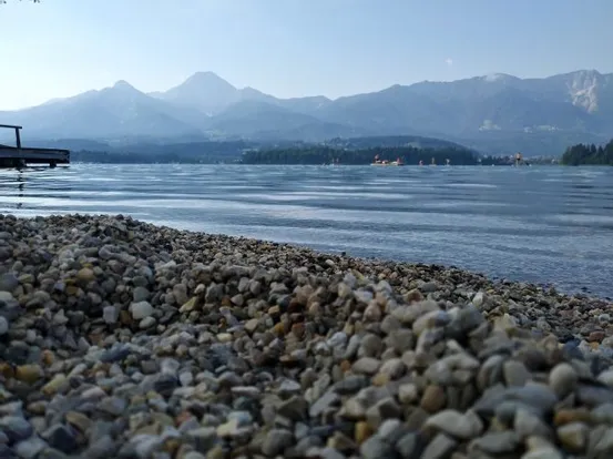 Kieselstrand an einem ruhigen See mit Bergpanorama im Hintergrund