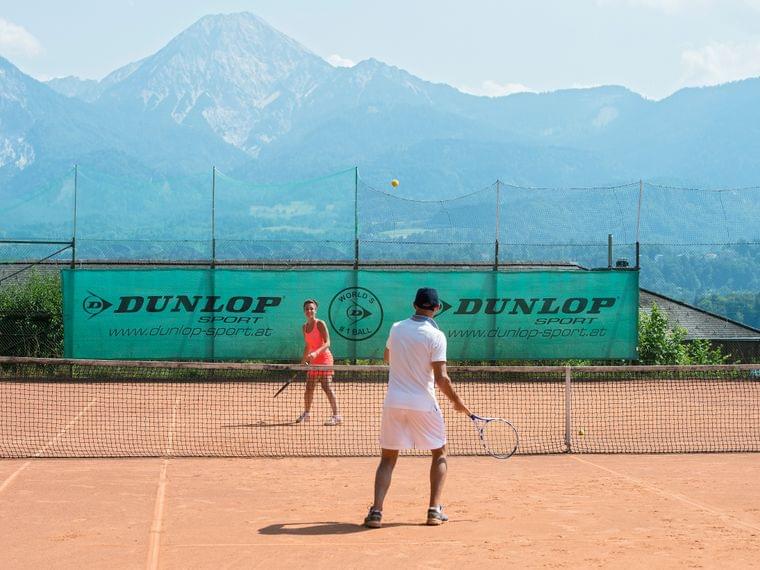Due persone giocano a tennis su un campo in terra battuta con montagne sullo sfondo