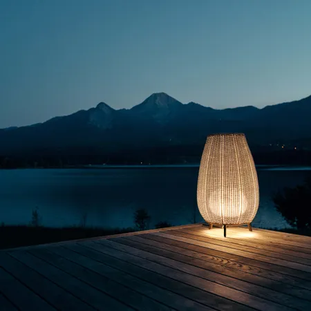 Lanterna da esterno illuminata su terrazza in legno con vista su lago e montagne al crepuscolo