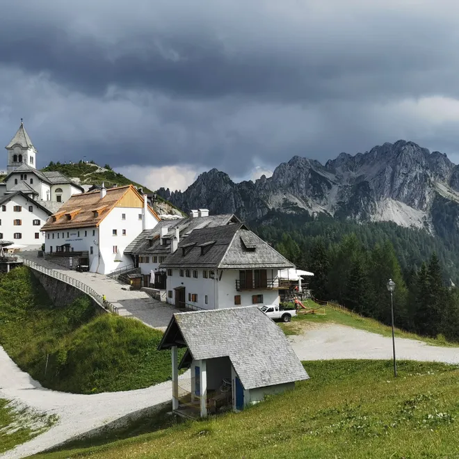 Bergdorf mit weißer Alpenkirche und Häusern unter dramatischem Wolkenhimmel