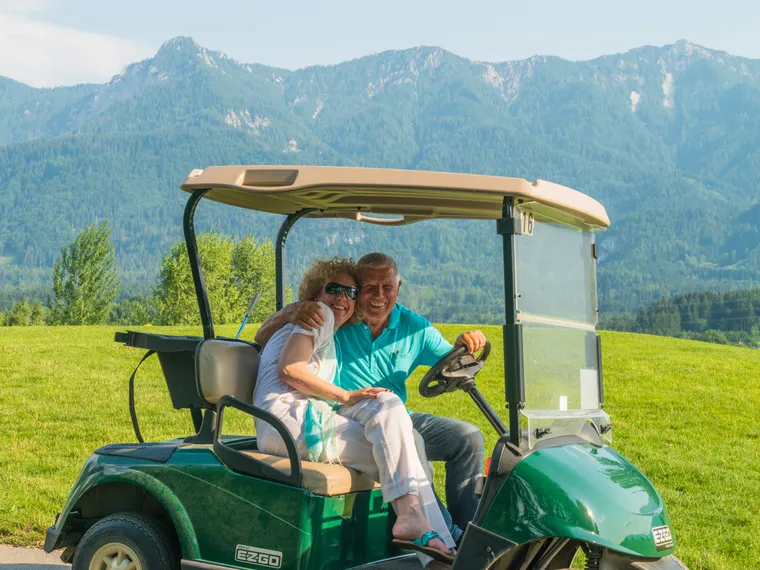 Smiling senior couple in golf cart with scenic mountain landscape background
