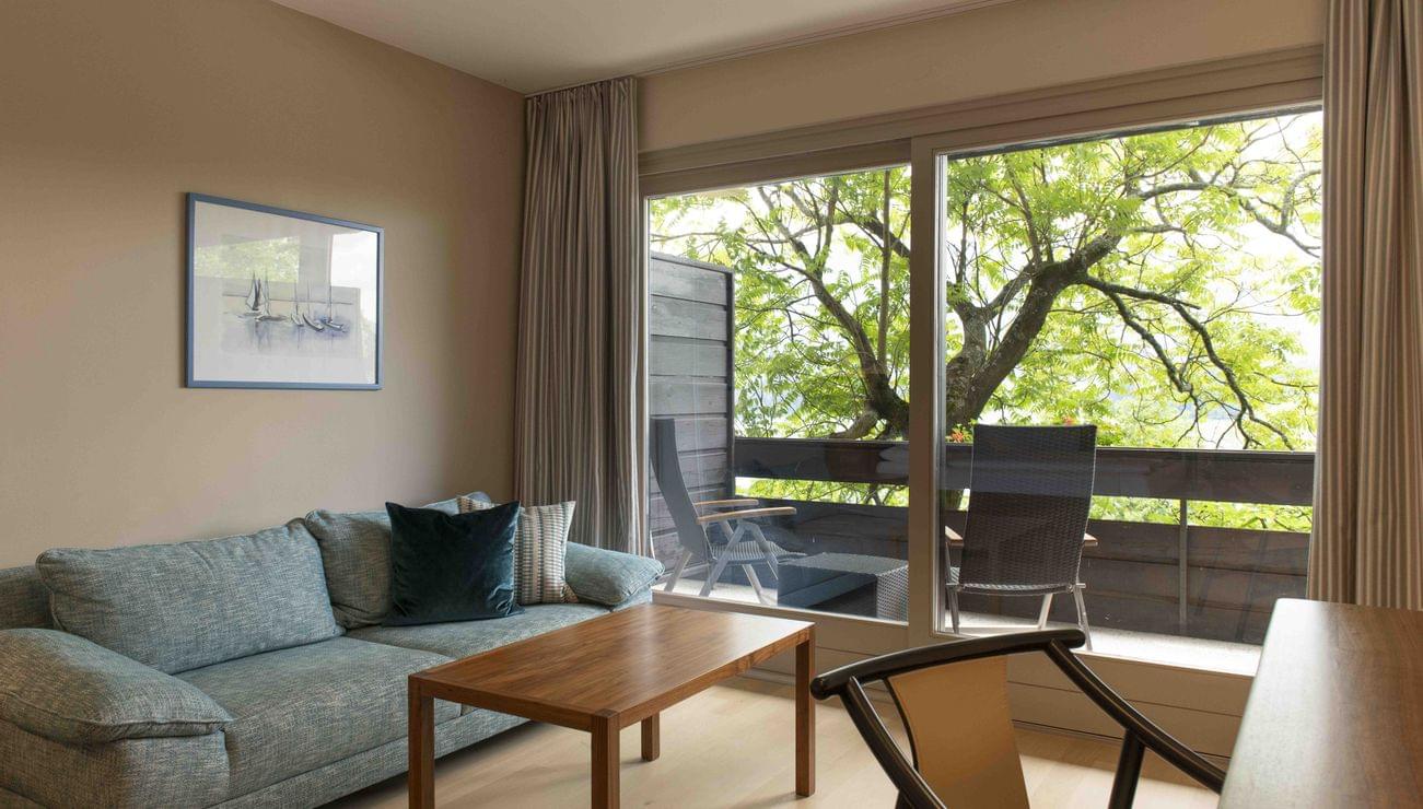 Modernes Wohnzimmer mit Sofa und Holztisch mit Blick auf Balkon und Bäume