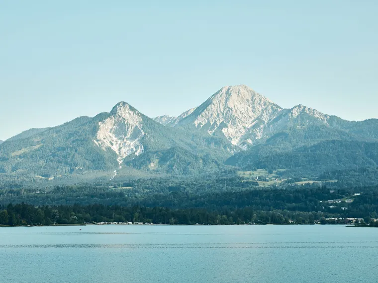 Mountain range with forest and lake in foreground under clear blue sky