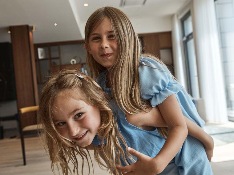 Due bambine sorridenti in vestiti blu che giocano insieme in un luminoso soggiorno moderno