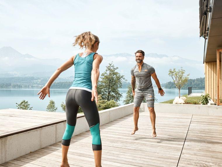 Couple doing outdoor workout on wooden terrace with mountain lake view