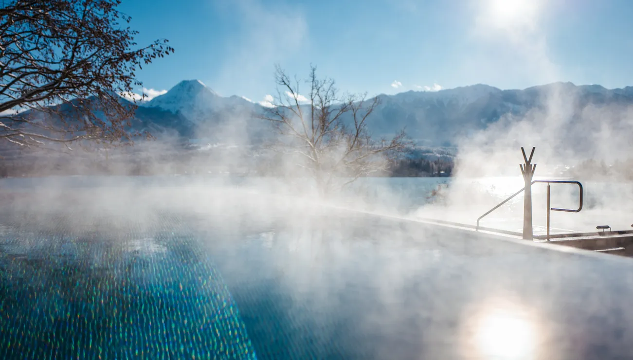 Vapore che sale da una piscina riscaldata all'aperto con vista sulle montagne innevate al sole