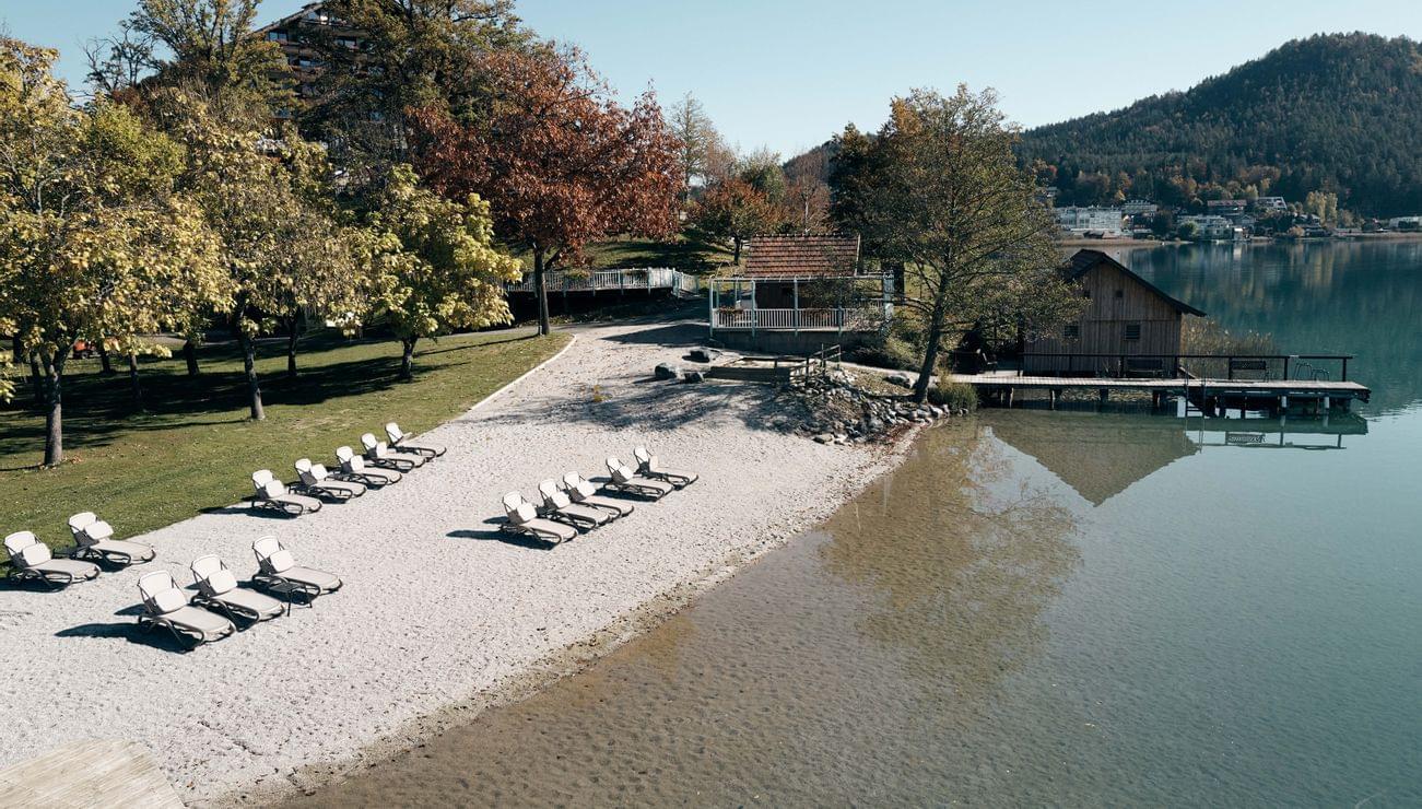 Empty sun loungers on a quiet lakeside beach with clear water and autumn trees