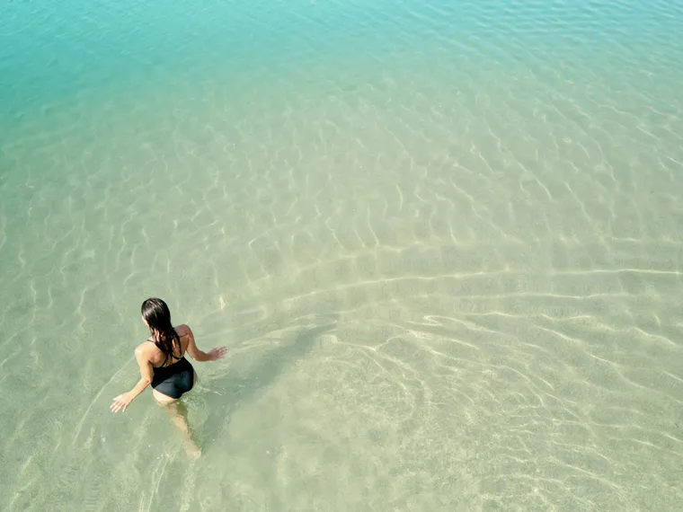 Woman in black swimsuit walking into clear turquoise sea at a tropical beach