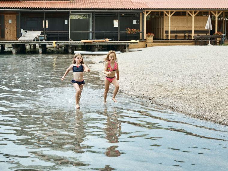 Due bambine in costume da bagno corrono nell'acqua bassa vicino a una cabina sul lago