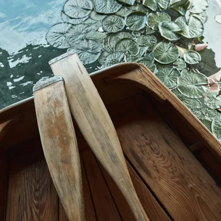 Holzboot mit Rudern neben Seerosen auf ruhigem Wasser