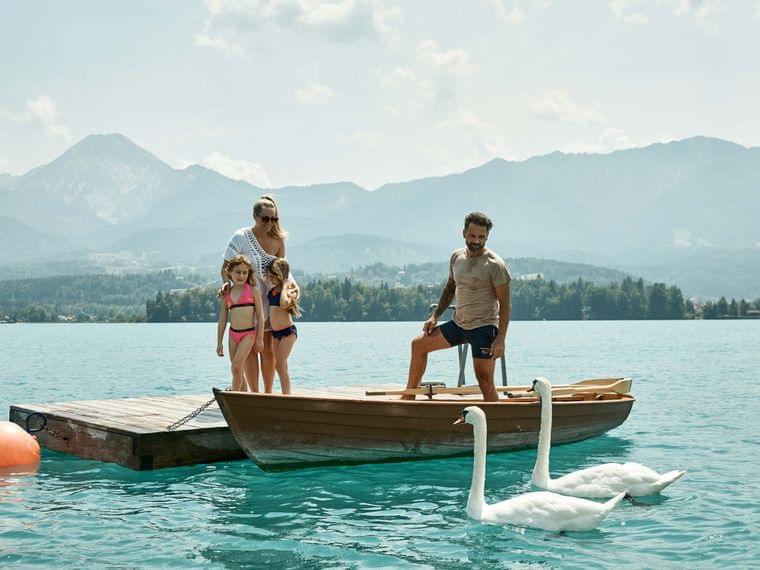 Famiglia su molo di legno con cigni su lago alpino turchese e sfondo montano
