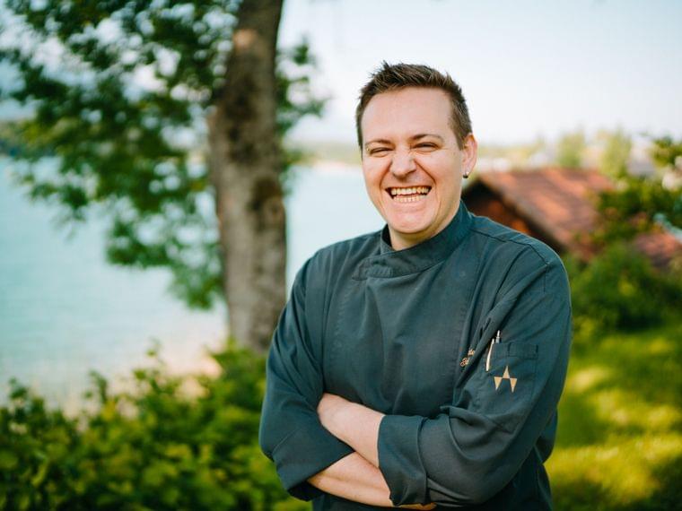 Smiling chef in dark uniform standing outdoors near a lake and trees