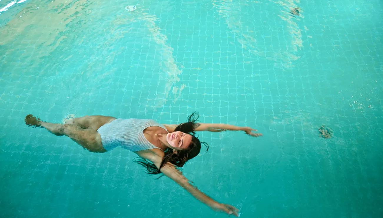 Frau treibt auf dem Rücken in einem klaren blauen Schwimmbecken