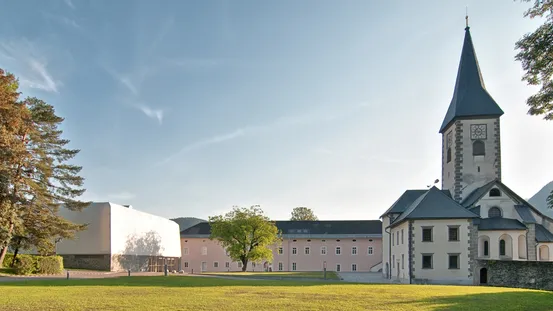 Historische Kirche mit hohem Turm und moderner Erweiterung in grünem Hof