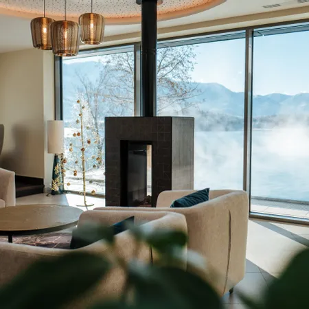 Moderne Lounge mit Kamin und Seeblick durch große Fenster in einem Luxushotel