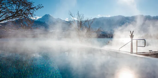 Steam rising from an outdoor heated pool with mountain view in winter sunshine