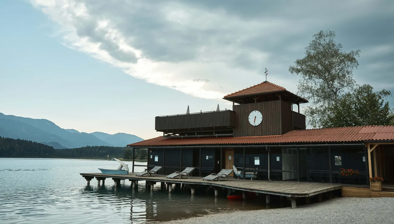 Holzbootshaus am See mit Uhrturm und Liegestühlen am ruhigen Wasser