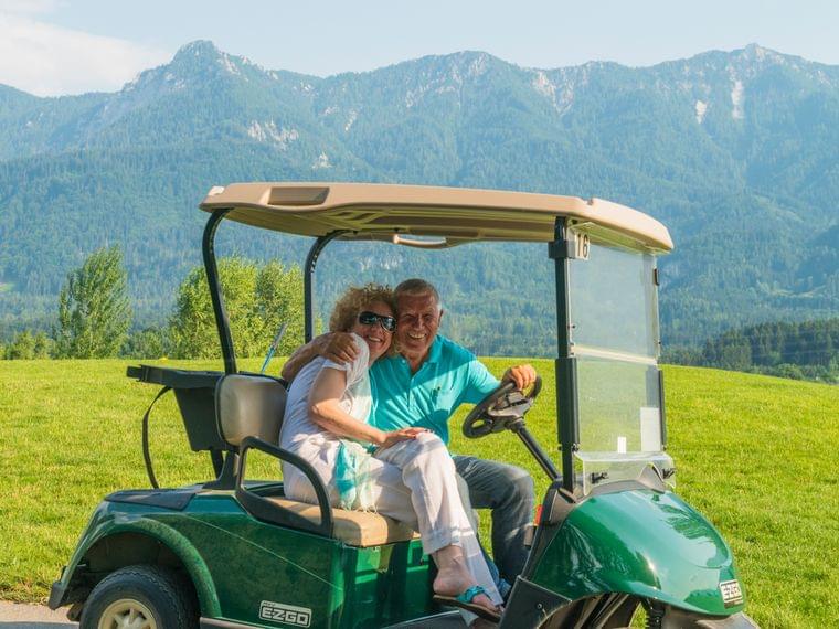 Lächelndes Seniorenpaar im Golfwagen vor malerischer Berglandschaft
