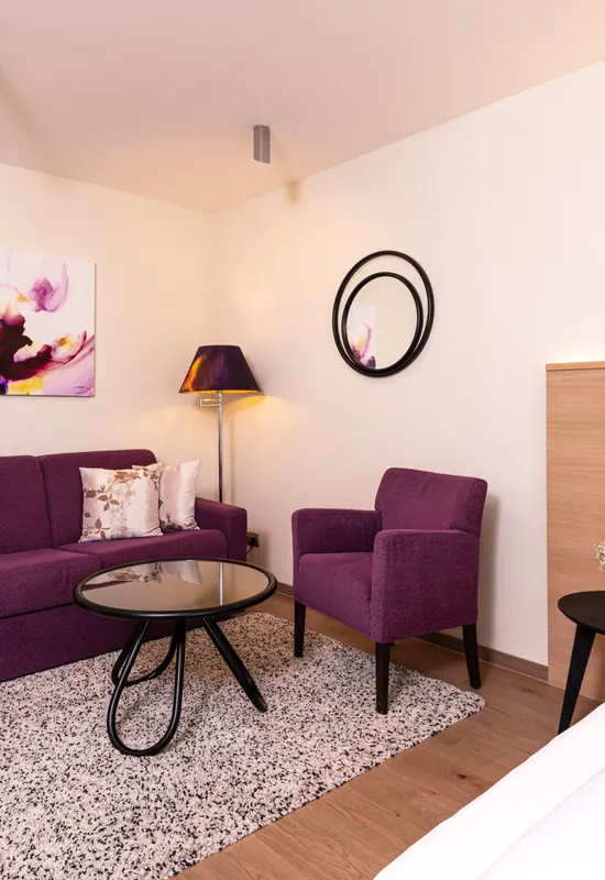 Modernes Hotelzimmer mit lila Sofa, Sessel und Dekor