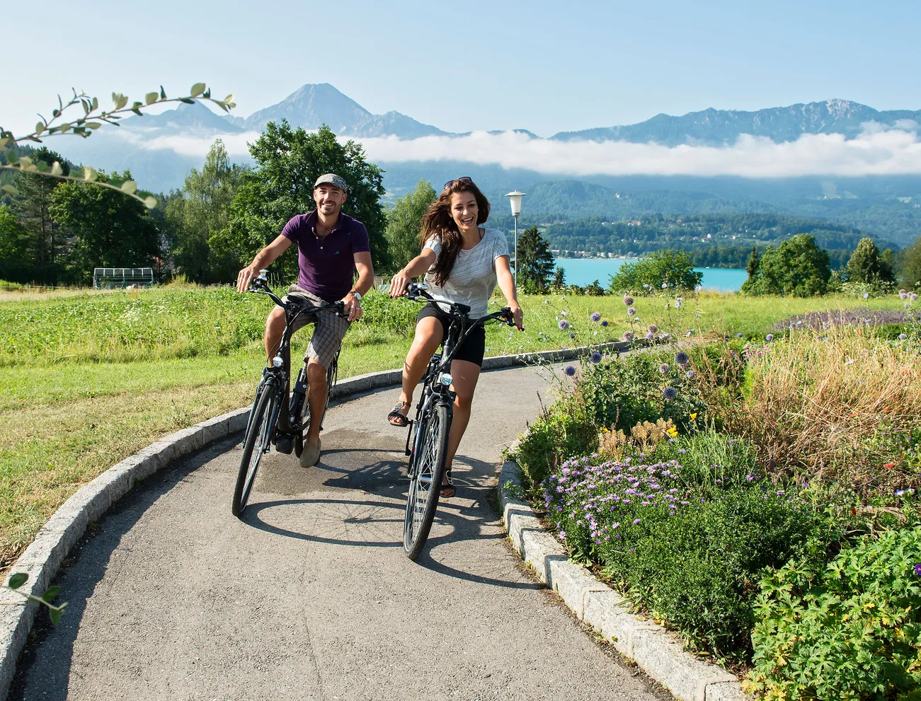 Paar fährt bei sonnigem Sommerwetter auf einem malerischen Weg nahe See und Bergen Fahrrad
