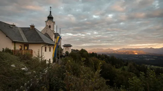 Kirche auf Hügel mit Blick ins grüne Tal und Gebirge bei Sonnenuntergang in Österreich
