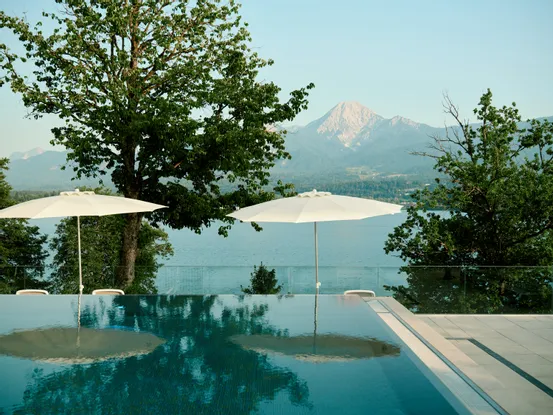 Infinity-Pool mit Sonnenschirmen und Blick auf See und Berge in malerischer Resortlage