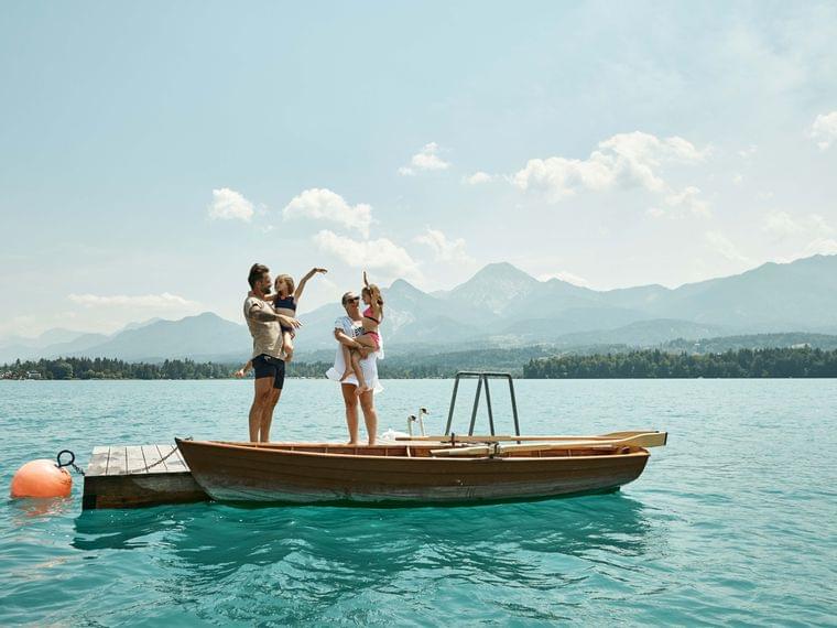 Family with children standing on boat docked on alpine lake with mountain view