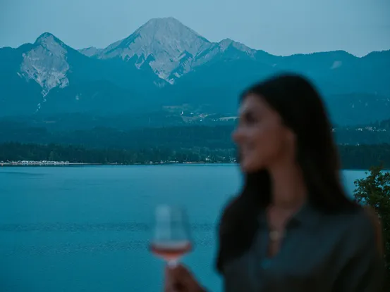 Frau mit Glas Roséwein vor See und Bergpanorama im Hintergrund